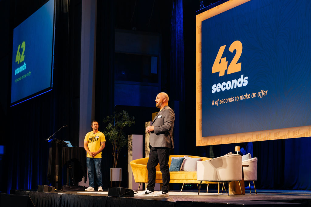 VP Benny Andrews and CSM Alex Tuttle stand on stage of Bushel Buddy Conference with a large display behind them